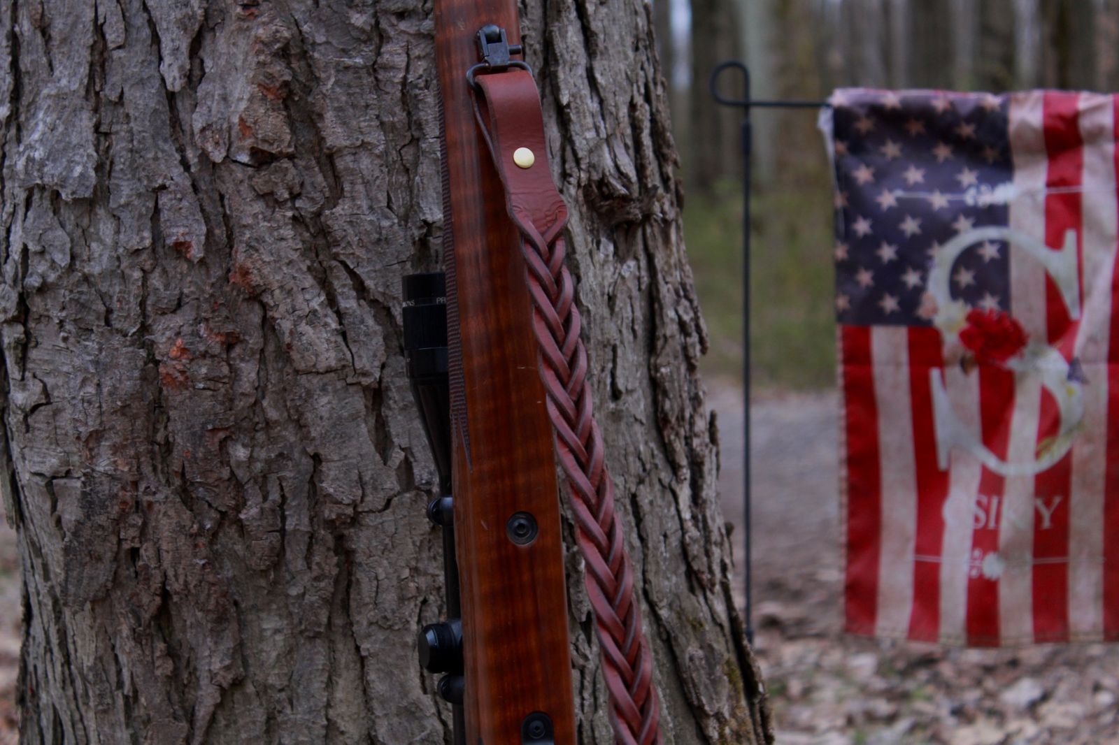 brown braided leather gun sling leaning on tree. braided leather gun sling made in the USA. Braided leather rifle sling, braided leather gun strap